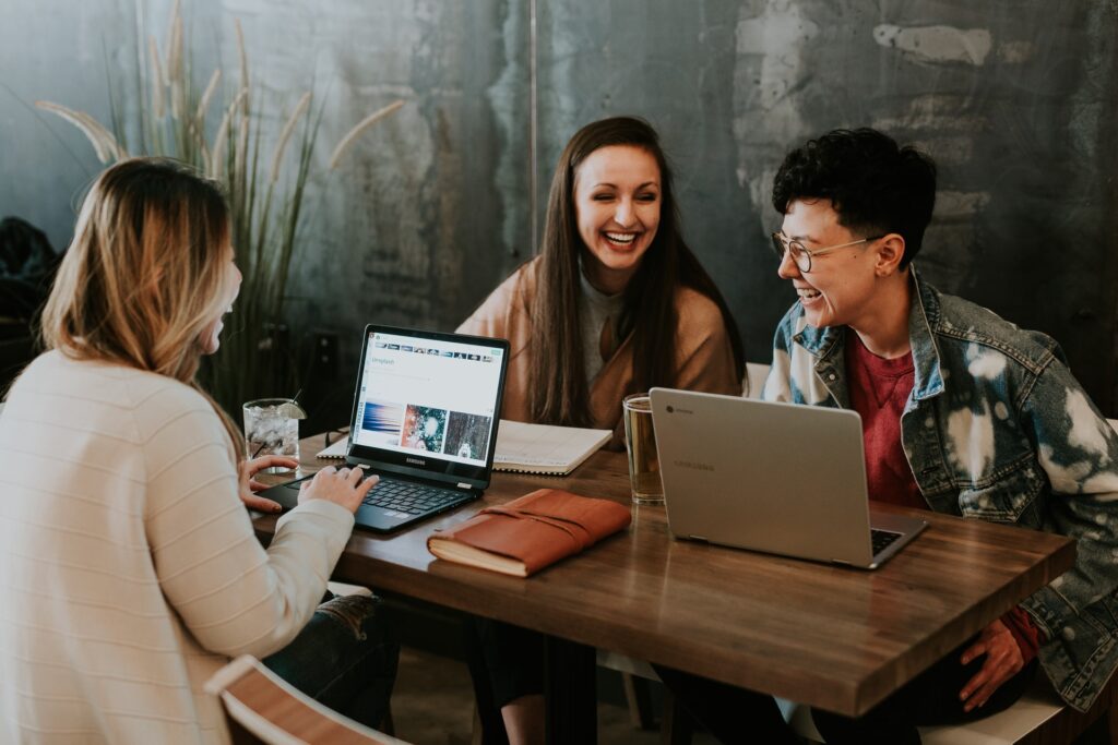 drei Studentinnen sehen sich Webdesign auf ihren Laptops an und lachen